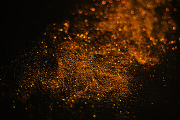 Fototapeta na wymiar Gold sand from sequins. Scattered sparkles on a black background. Blurred bokeh background