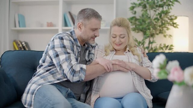 Happy future parents feeling baby movements, holding hands on pregnant belly