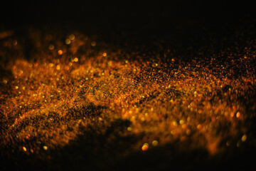 Gold sand from sequins. Scattered sparkles on a black background. Blurred bokeh background