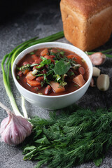 Bean soup with herbs in a white bowl with fresh rye bread and garlic on a slate table on a dark background