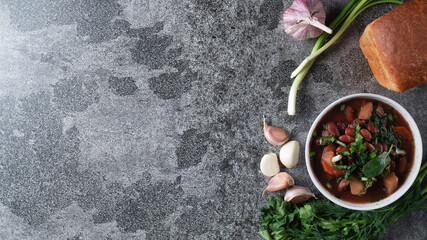 Fototapeta na wymiar Bean soup with herbs in a white bowl with fresh rye bread and garlic on a slate table on a dark background, top view, space for text