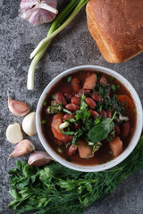 Bean soup with herbs in a white bowl with fresh rye bread and garlic on a slate table on a dark background, top view, space for text