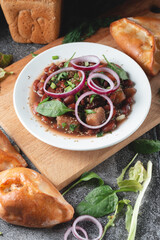 Bean soup with herbs and red onion rings in a white plate with fresh rye bread and garlic on a slate table on a dark background.