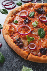 Traditional Italian pepperoni pizza with onions, herbs, tomatoes and cheese on a dark slate table.