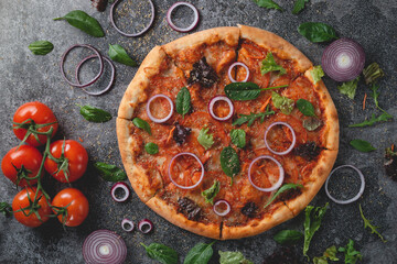Fototapeta na wymiar Traditional Italian pepperoni pizza with onions, herbs, tomatoes and cheese on a dark slate table.