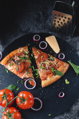 Slices Traditional Italian pepperoni pizza with tomatoes, grated metal cheese, onions and herbs, on a table of dark slate on a black background..