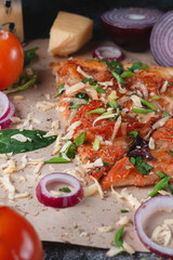 Slices Traditional Italian pepperoni pizza with tomatoes, grated metal cheese, onions and herbs, on a dark slate table with paper .
