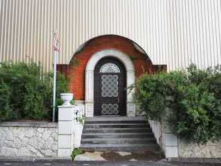 Porch with an arched iron door with a wrought pattern, bushes on the sides and a metal profile flap