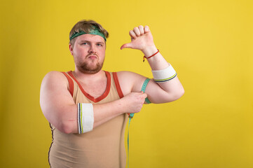 A funny, cheerful fat man in sportswear measures his arms. Overweight man goes in for sports....