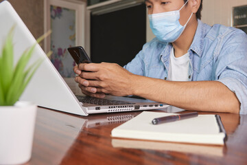 Fototapeta premium Zoom View Casual Businessman in Denim or Jeans Shirt Wear Face Mask Using Smartphone to Chat Online in Coffee Shop. Casual Businessman with Technology in Covid 19 Situation