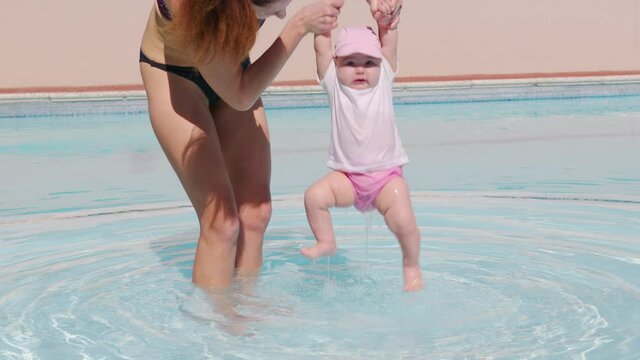 A mother and a baby in an outdoor swimming pool. Mother kissing baby toddler at the swimming pool. Mom embracing holding and caring for infant.