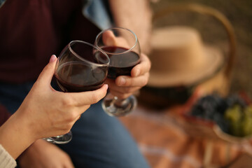Man and woman hands are holding glasses with red wine. Picnic date in the summer.