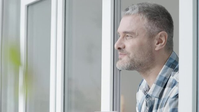 Smiling grey-haired man drinking tea, looking outside, coffee break at work