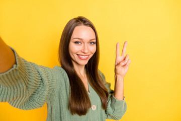 Photo portrait of woman showing v-sign taking selfie isolated on vivid yellow colored background