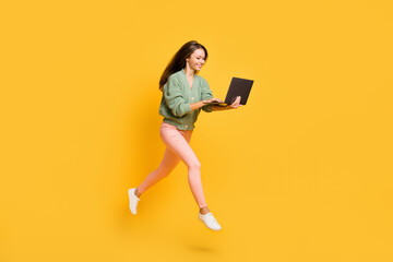 Full size profile side photo of young happy cheerful smiling girl run in air work in laptop isolated on yellow color background