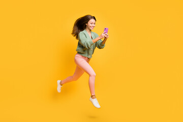 Fototapeta na wymiar Full size profile side photo of young happy excited crazy girl run in air using smartphone isolated on yellow color background