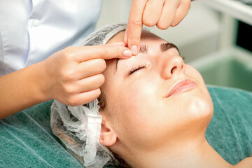 Beautician's hands make massage on eyebrow for a woman while a facial massage in cosmetology clinic center