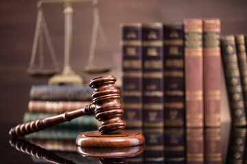 Law theme. Judge chamber. Judge’s gavel, scale and collection of legal books on the brown desk and the brown background.