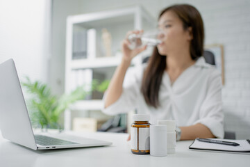 Business woman drink water. She felt sick. A close up of a medicine bottle on the desk.