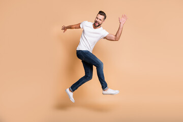 Fototapeta na wymiar Full length body size view of attractive funky cheerful guy jumping having fun dancing running isolated over beige pastel color background