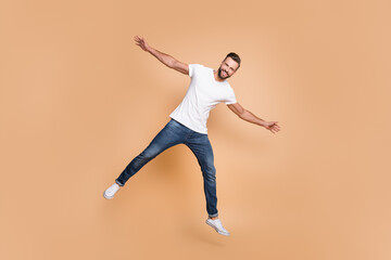 Fototapeta na wymiar Full length body size view of attractive glad cheerful guy jumping having fun fooling isolated over beige pastel color background