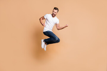 Fototapeta na wymiar Full length body size view of nice cheerful guy jumping having fun victory triumph isolated over beige pastel color background