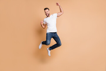 Fototapeta na wymiar Full length body size view of nice tall cheerful macho guy jumping rejoicing having fun isolated over beige pastel color background