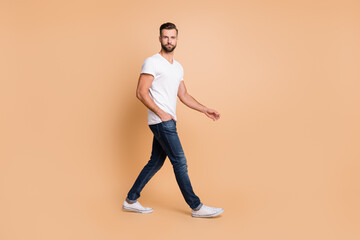 Fototapeta na wymiar Full length photo of young handsome man confident serious go walk step hand in pocket isolated over beige color background