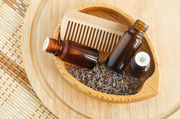 Small wooden bowl with dry lavender, bottles with essential oil and wooden hair brush. Aromatherapy, homemade spa, natural hair care concept, Top view, copy space.