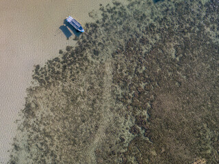 Aerial view of tropical island coastline, clean ocean with coral reefs and fishing boat