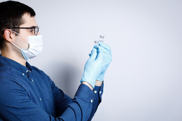 The doctor is looking at vaccine in his hands in  blue disposable gloves.Vaccine phials for coronavirus covid-19. Prevention and immunization concept.
