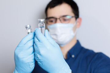 Close up of doctor hands wearing blue disposable gloves and showing vaccine phials for coronavirus covid-19. Hand holding vial dose vaccine for vaccine, prevention and immunization concept.
