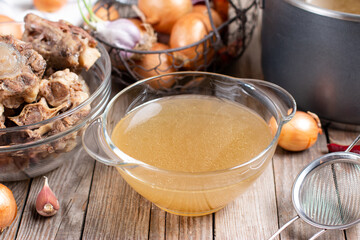 Bowl with beef broth, bones and fresh vegetables on a wooden table, paleo diet