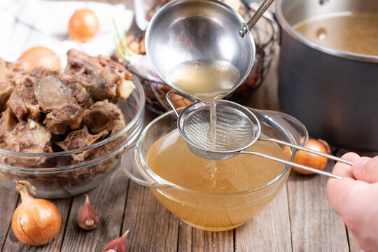 Passing the bone broth through a sieve. Concentrated Bone Broth in a bowl on the table