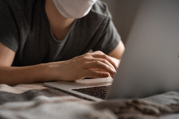 The man in the mask works with the laptop lying on the bed