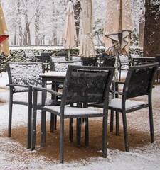 Naklejka premium tables and chairs on a terrace of an empty restaurant with no client because of virus and snowstorm in garden with umbrellas