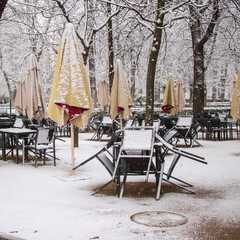 Obraz premium tables and chairs on a terrace of an empty restaurant with no client because of virus and snowstorm in garden with umbrellas