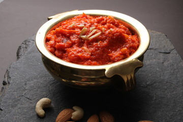Gajar ka halwa is a carrot-based sweet dessert pudding from India. Garnished with Cashew almond nuts and Served in brass bowl.