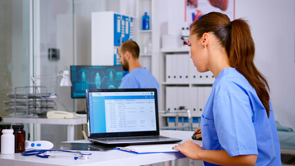 Doctor assistant checking list diagnosed of patients, writing on clipboard with x-ray and medical equipment around. Physician working in hospital making appointments and analysing patient registration - obrazy, fototapety, plakaty