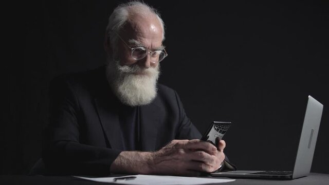 Surprised old businessman reading news at smartphone in office with astonishment