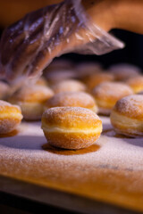 hand pouring icing sugar on doughnut