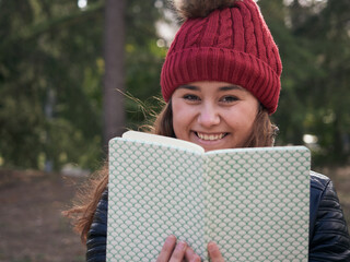 Shallow focus shot of a young caucasian female wearing a red winter hat reading a book in the park