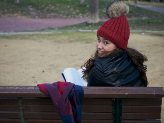 Young caucasian female reading book while sitting on a wooden bench in the park