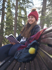 Young caucasian female reading book while sitting on a wooden bench in the park