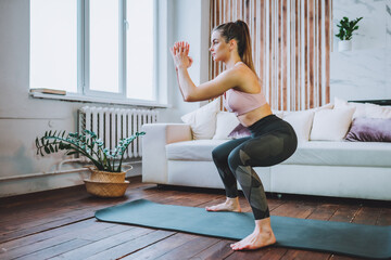Young fit woman in sportswear do squat exercise indoors in living room. Online indoors workout....