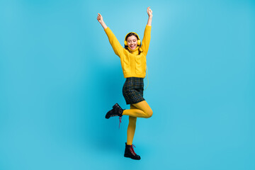 Full length photo of adorable lucky woman dressed yellow pullover earphones rising hands dancing isolated blue color background