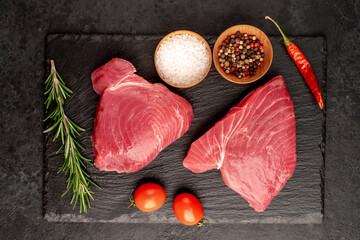 Fresh raw tuna steaks with rosemary and spices on a stone background

A