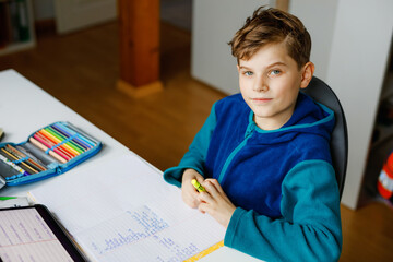 Naklejka na ściany i meble School kid boy learning at home with tablet for school. Adorable child making homework and using pad and modern gadgets. Home schooling and distance learn concept.