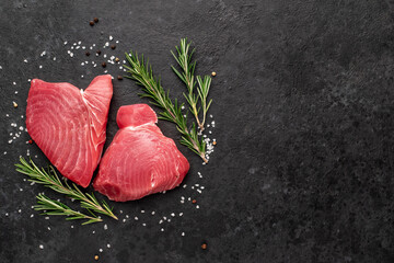 Fresh raw tuna steaks with rosemary and spices on a stone background with copy space for your text