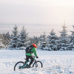 Mountain biker riding on the snow. A daring man on the top of the high mountain go down on a summer sunny day. Athlete On Racing Bike Cycling Through Mountains. Winter Mountain Bike Crossing